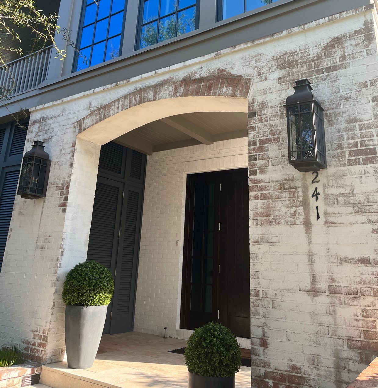 Renovated arched brick entry with a dark wood front door and lanterns
